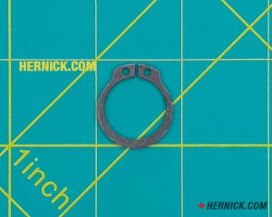 Black spring steel external retaining ring (C-ring/circlip) with two installation eyelets on a green background with yellow grid markings.