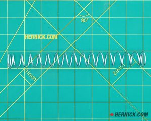 Heavy-duty steel arm restraint spring on a green background with yellow grid markings.