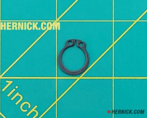 Black steel external retaining ring (circlip) with two installation eyelets on a green background with yellow grid markings.